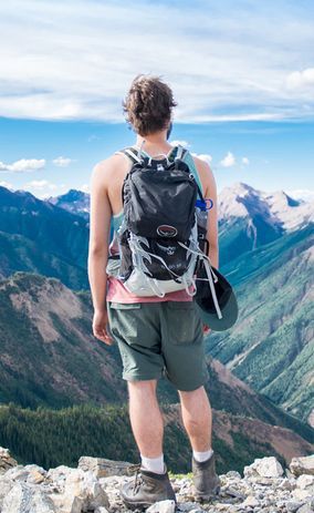 Мужчина с рюкзаком стоит на вершине горы и смотрит вдаль.