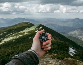 Рука с компасом на фоне горы.
