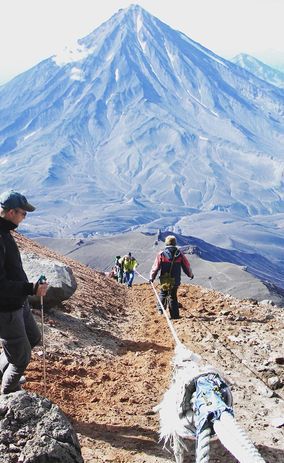 Группа туристов восходит на вершину, держась за веревку.