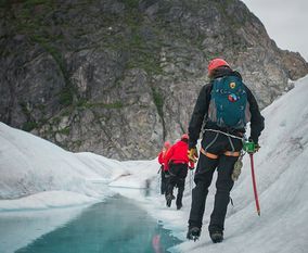 Группа туристов идет по снегу вдоль горной речки.